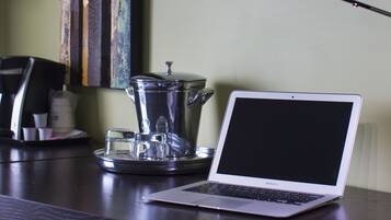 A laptop on a dark wooden desk with a coffee maker and cups.