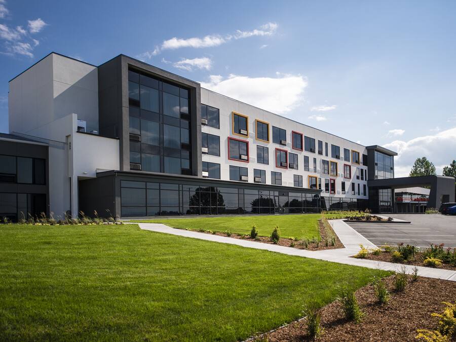 A modern building with large windows, a parking lot, and a well-maintained lawn.