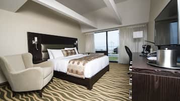 A hotel room with a large bed, a sofa, a desk with a TV, and a view of the city.