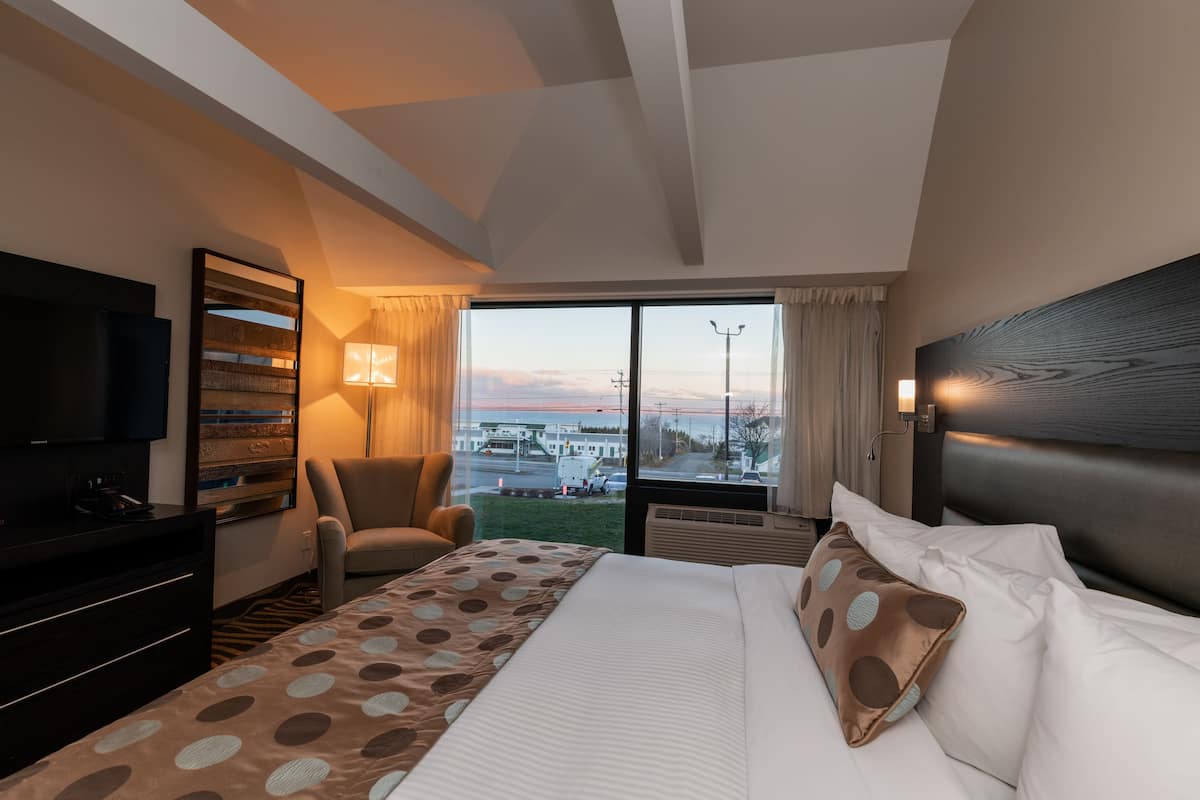 A hotel room with a bed, a TV, a chair, and a view of the cityscape.