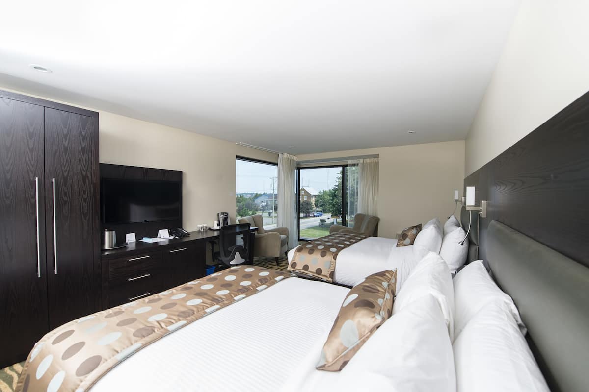A hotel room with two beds, a desk, a TV, and a view of the outdoors.