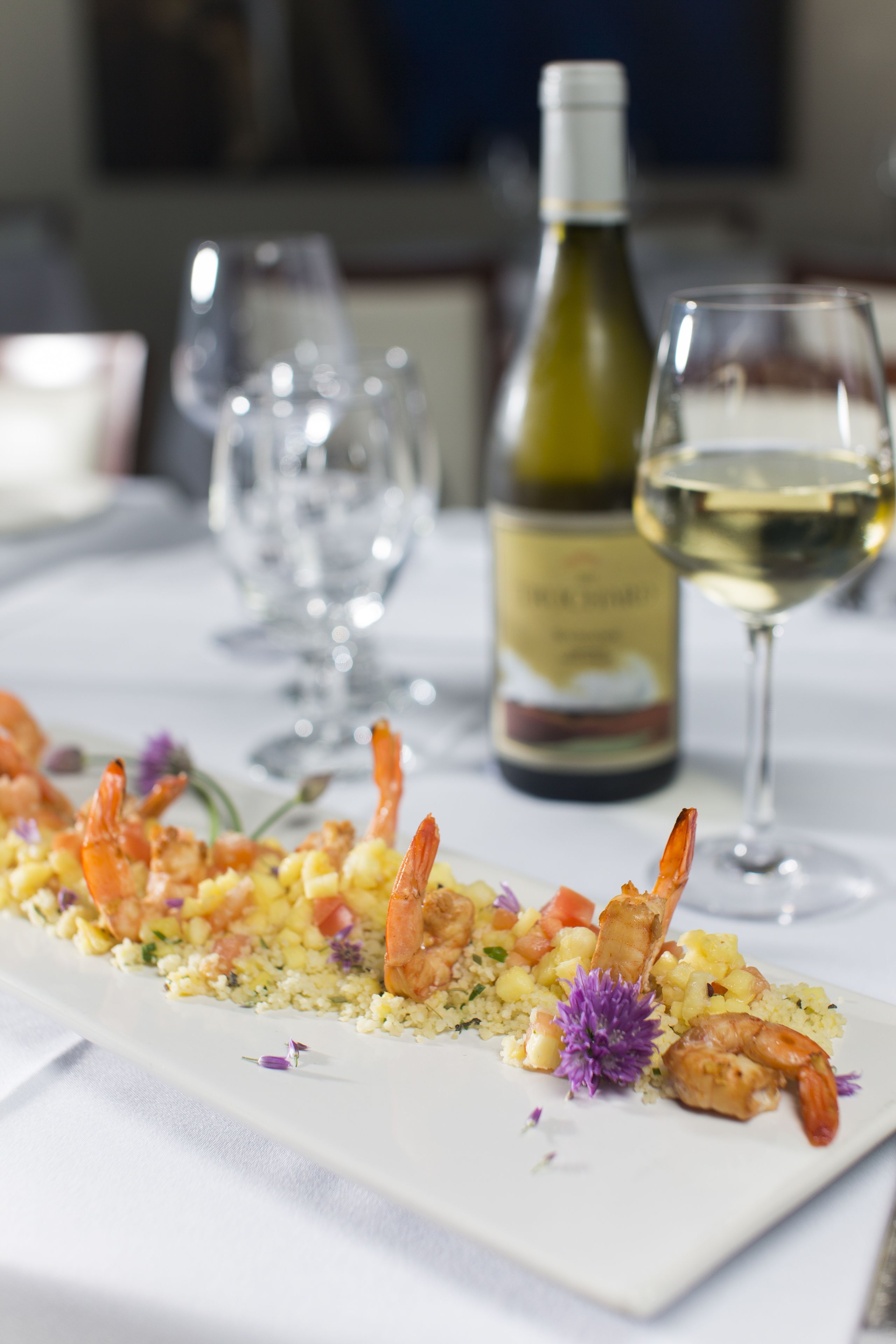 A dining table with a seafood dish, wine glasses, and a bottle of wine.