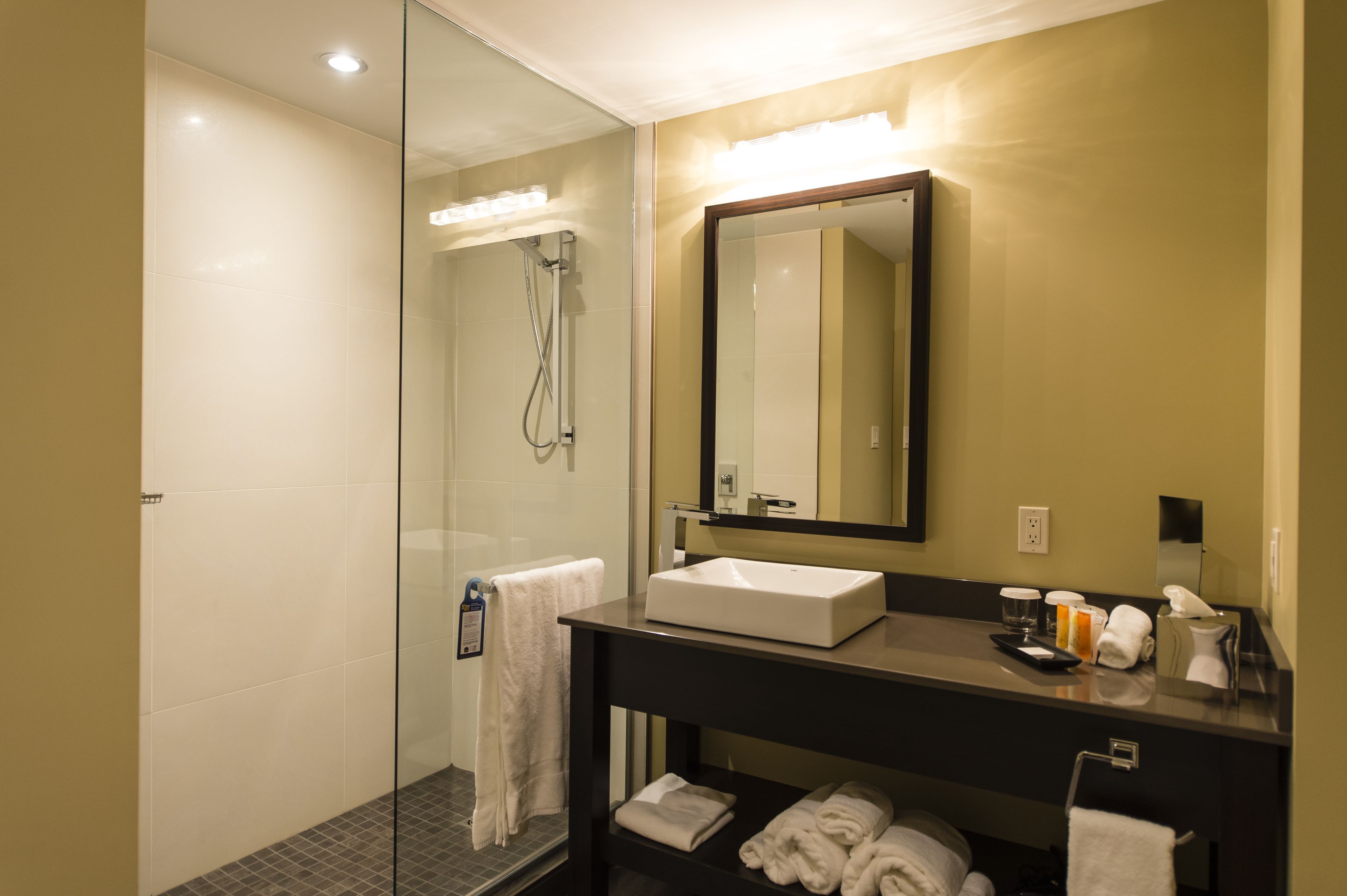 A modern bathroom with a glass-enclosed shower, a large mirror, and a black vanity with a white sink.