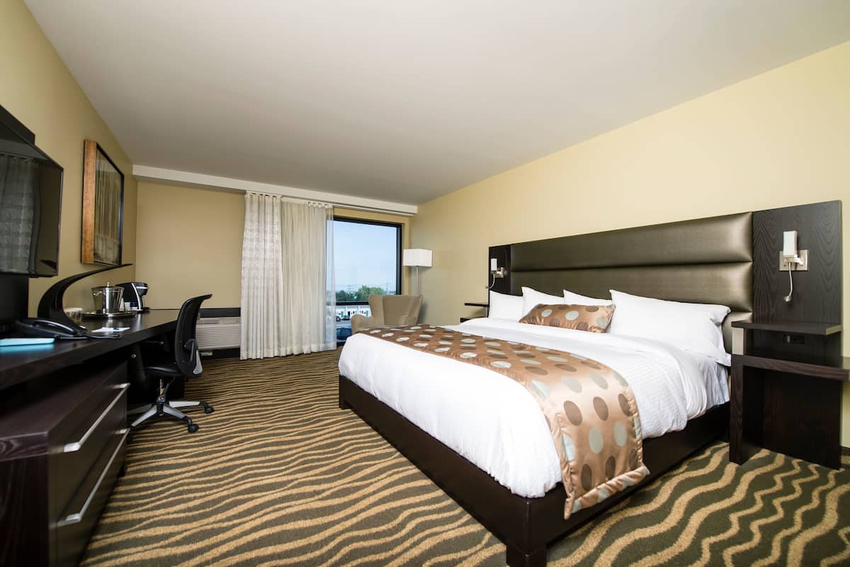 A hotel room with a large bed, a desk with a computer, a chair, and a window with curtains.