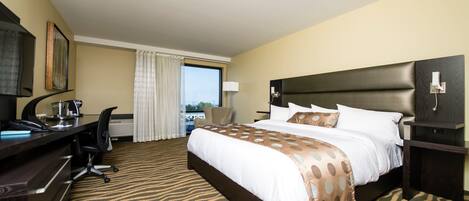 A hotel room with a large bed, a desk with a computer, a chair, and a window with curtains.