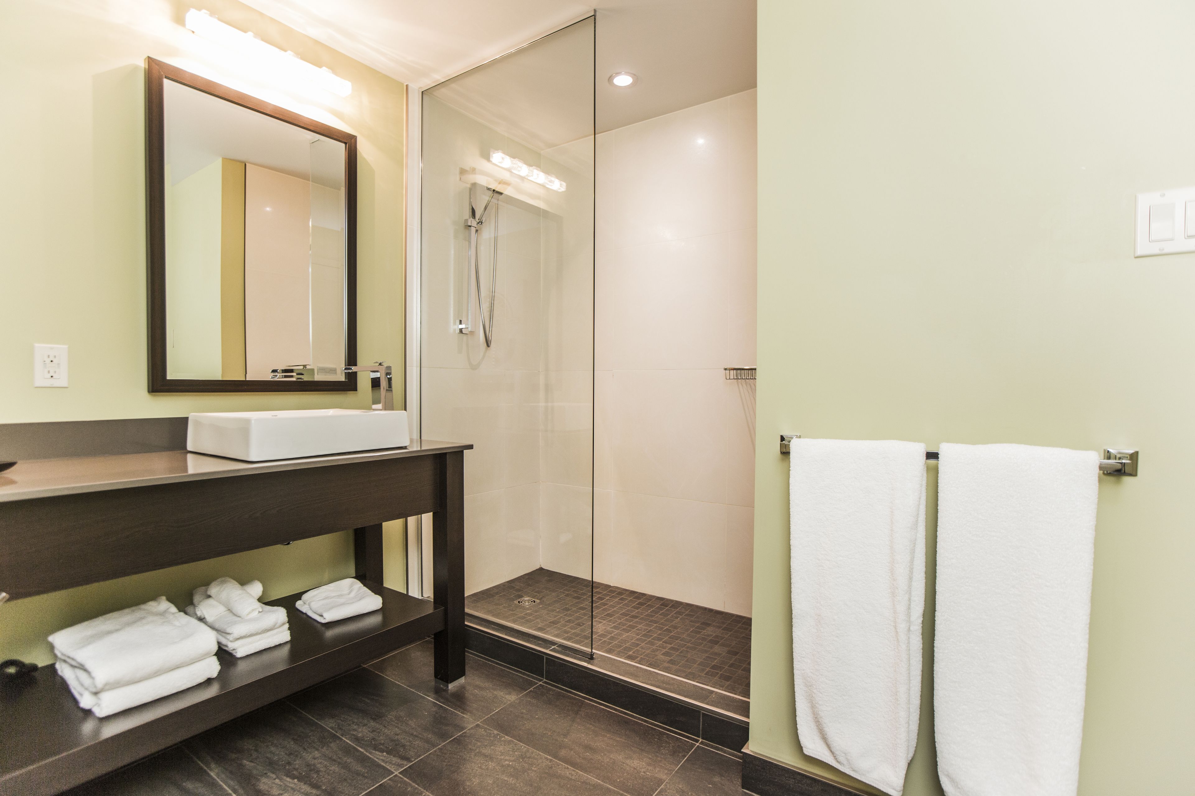 A modern bathroom with a large mirror, a sink, a shower, and two towels hanging on a rack.
