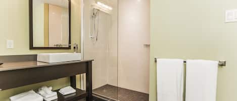 A modern bathroom with a large mirror, a sink, a shower, and two towels hanging on a rack.