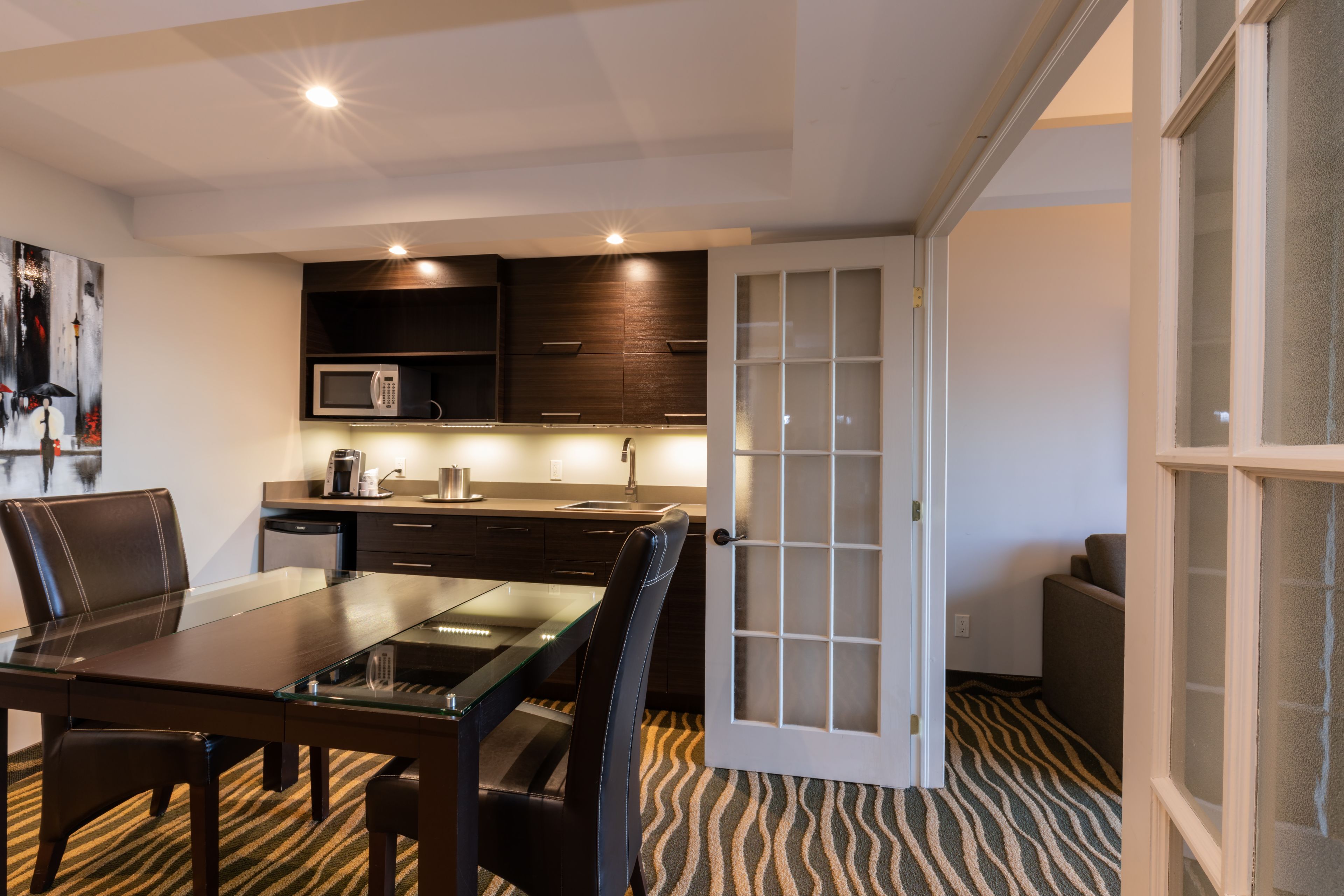 A modern kitchen with dark wood cabinets, a microwave, and a glass dining table with chairs.