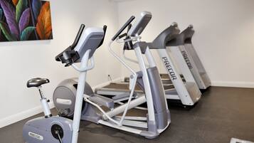 Et fitnessrum med motionscykler og løbebånd, et billede hængt på væggen, og et gråt gulv.