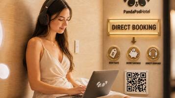 Une personne utilise un ordinateur portable dans une pièce qui contient un lit, un panneau fixé au mur pour les réservations directes et un code QR.