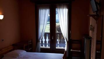 Quarto de hotel com duas camas, uma varanda com guarda-corpo e uma televisão na parede.
