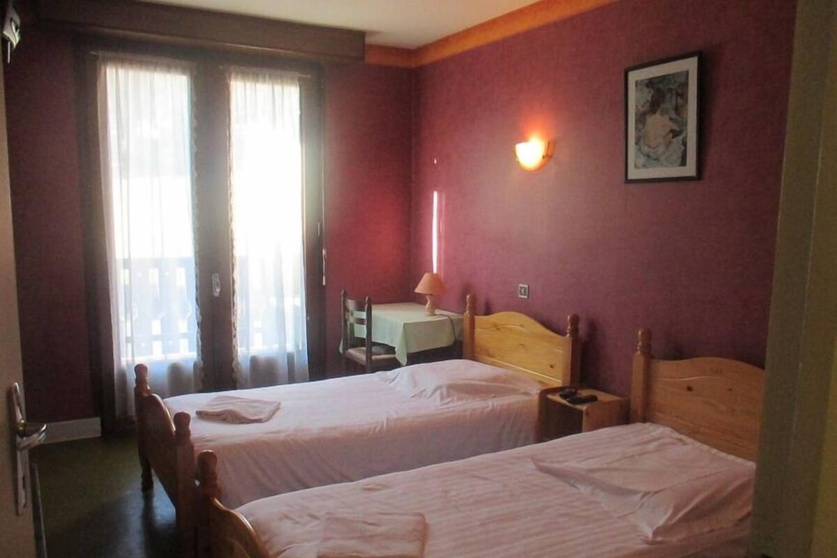 A hotel room with two single beds, a desk with a chair, a lamp, and a window with curtains.