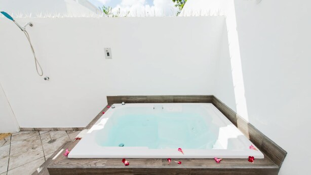 Un bain à remous rectangulaire, bordé de bois, entouré d’un mur blanc et d’une clôture blanche.