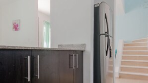 Une cuisine moderne avec des meubles de couleur sombre, un réfrigérateur en acier inoxydable et un plan de travail de couleur claire.