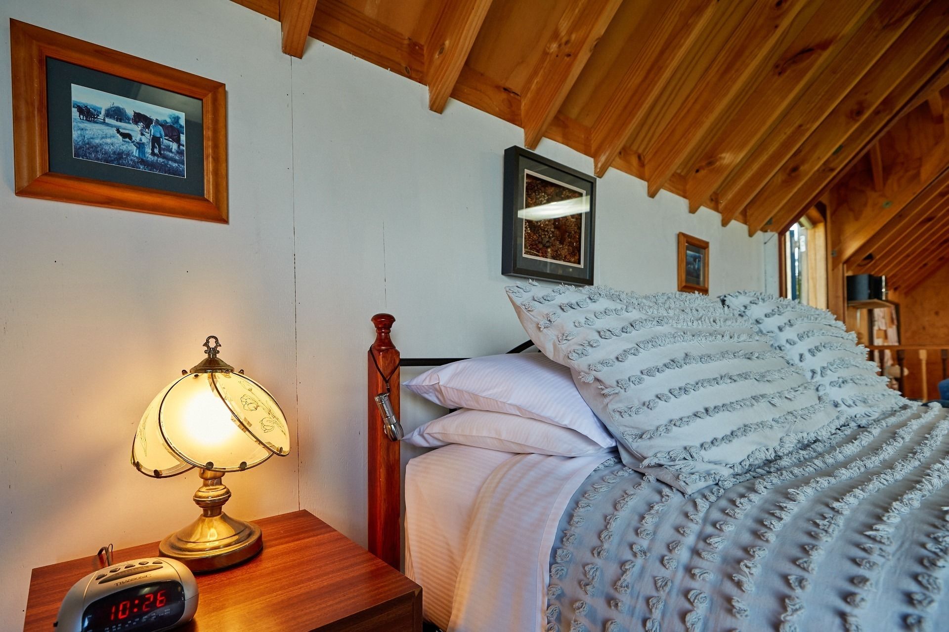 A bedroom with a wooden headboard, a bedside lamp, a digital clock, and framed pictures on the wall.