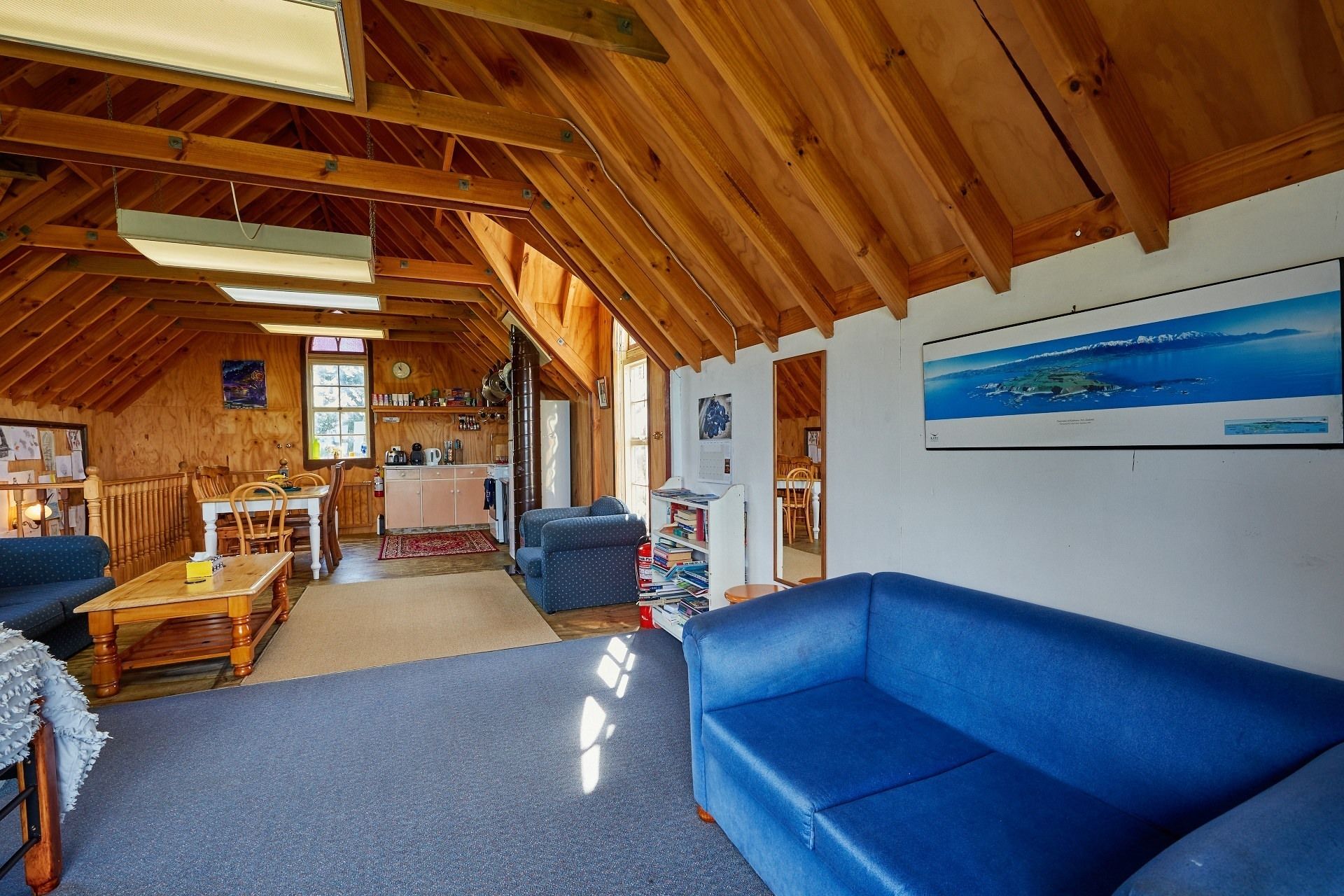 Een gezellige woonkamer met houten vloeren, een blauwe bank, een houten eettafel en een keuken met een koelkast en boekenkasten.