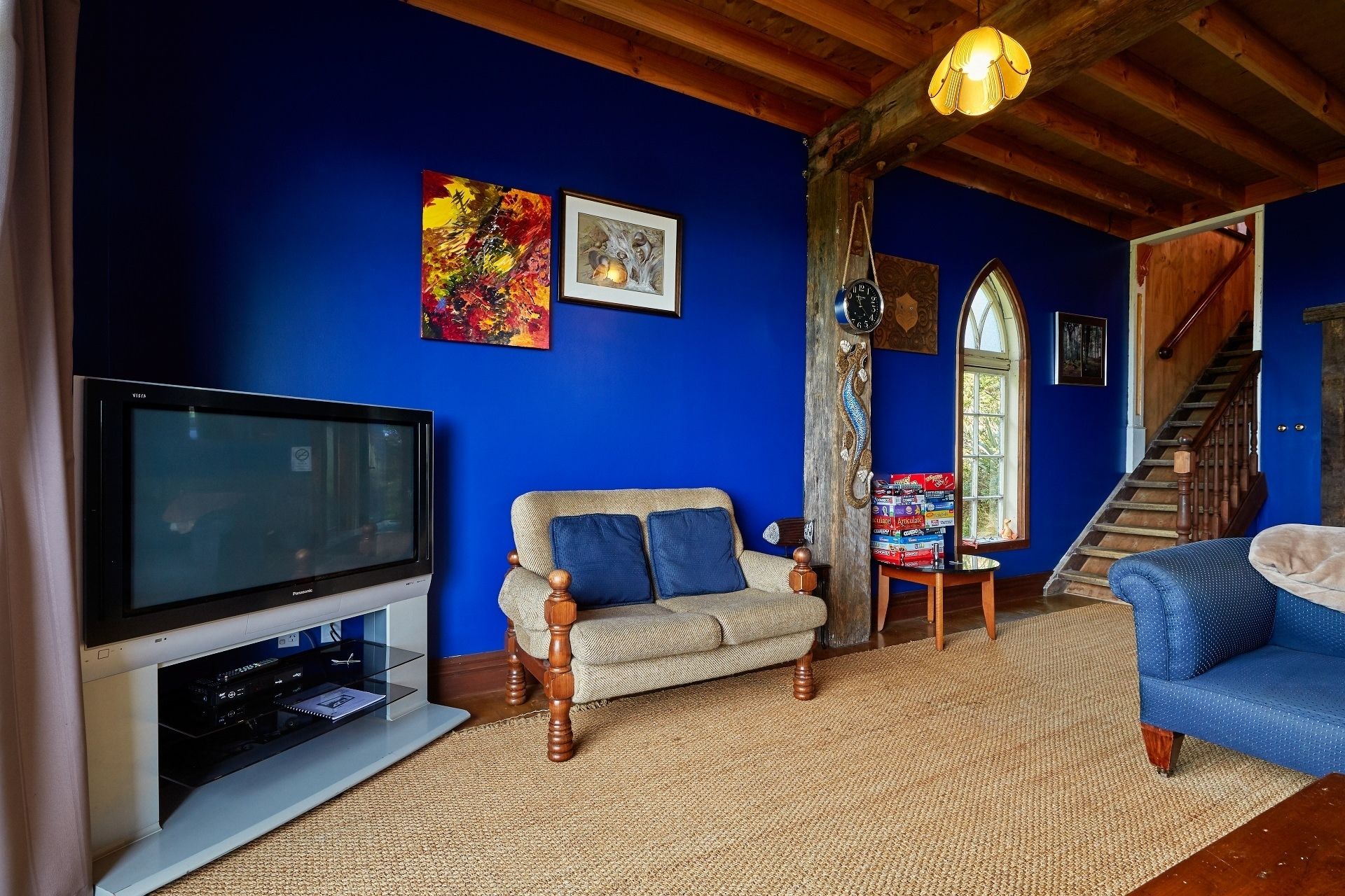 Un salon avec une télévision, un canapé et un fauteuil. Un escalier mène à un autre niveau.