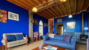Un salon chaleureux aux murs bleus, avec des poutres en bois, une cheminée et un escalier menant à un autre niveau.