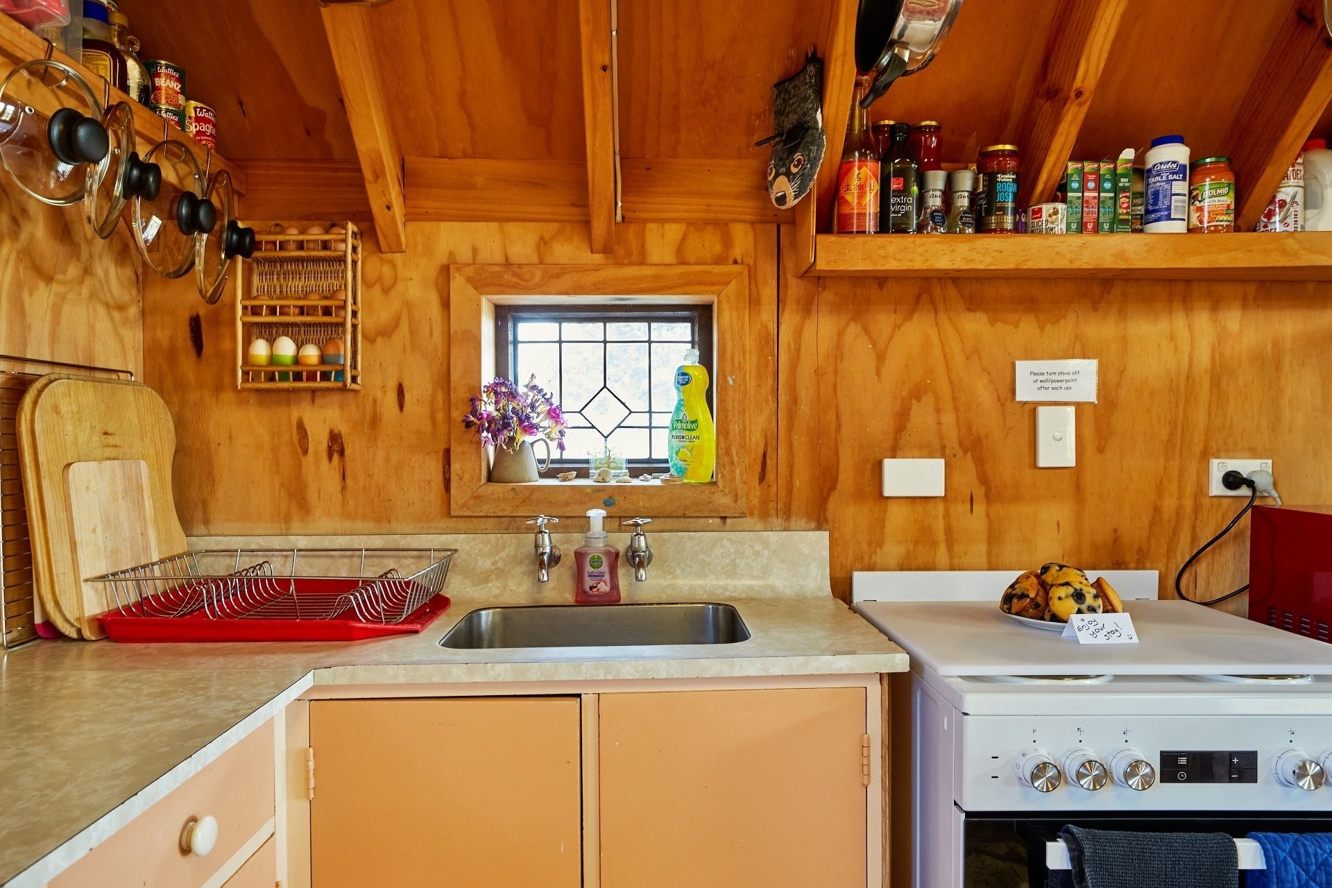 Una cocina compacta con armarios de madera, un lavamanos, una estufa y varios utensilios de cocina en estantes.