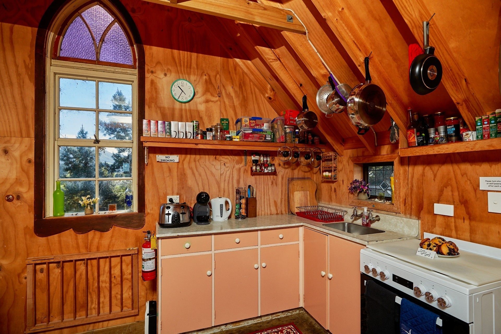 A cozy kitchen with wooden walls, a large window, and various kitchen appliances.
