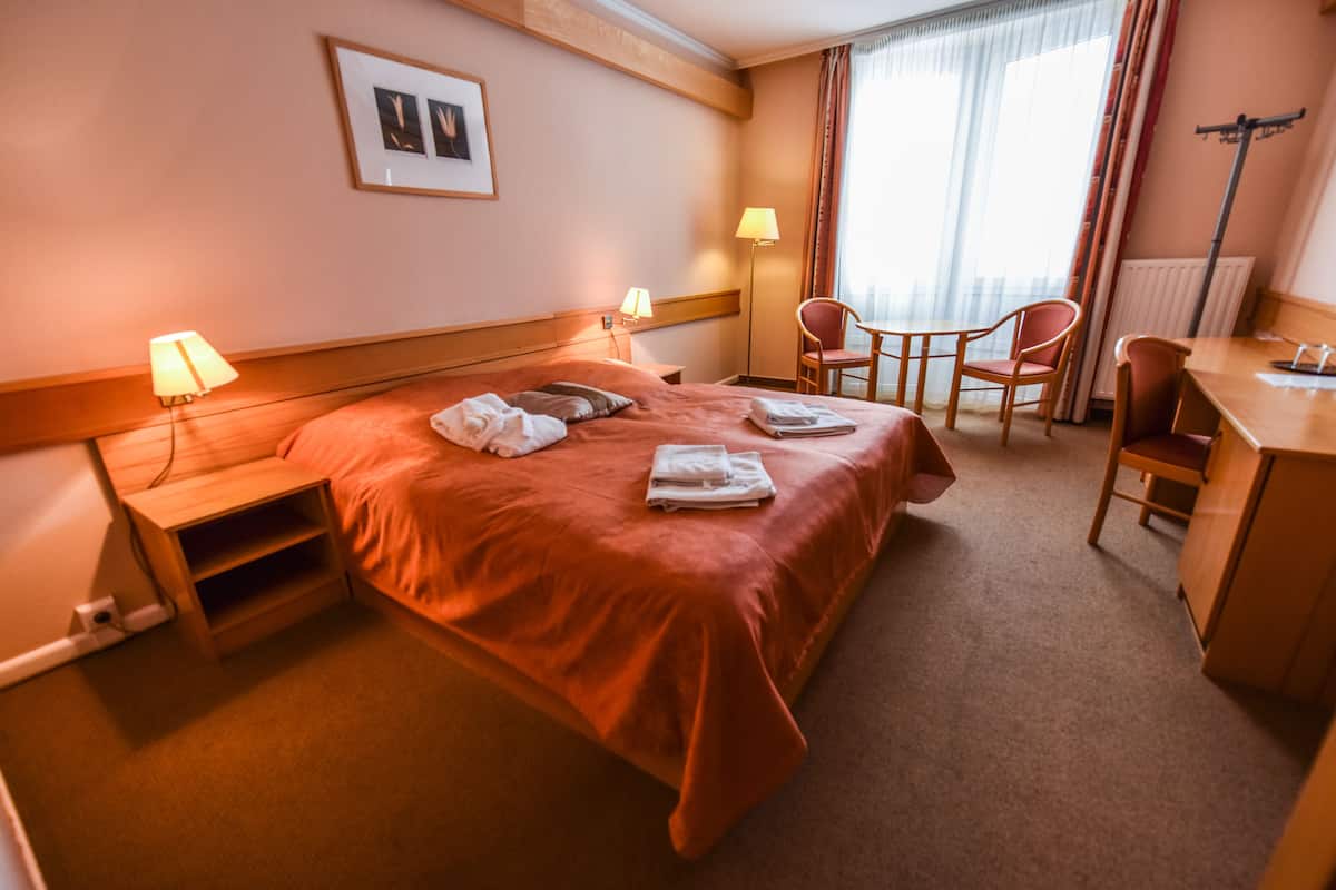 Ein Hotelzimmer mit einem Bett, zwei Nachttischen, einem Schreibtisch, einem Sessel und einer Lampe.