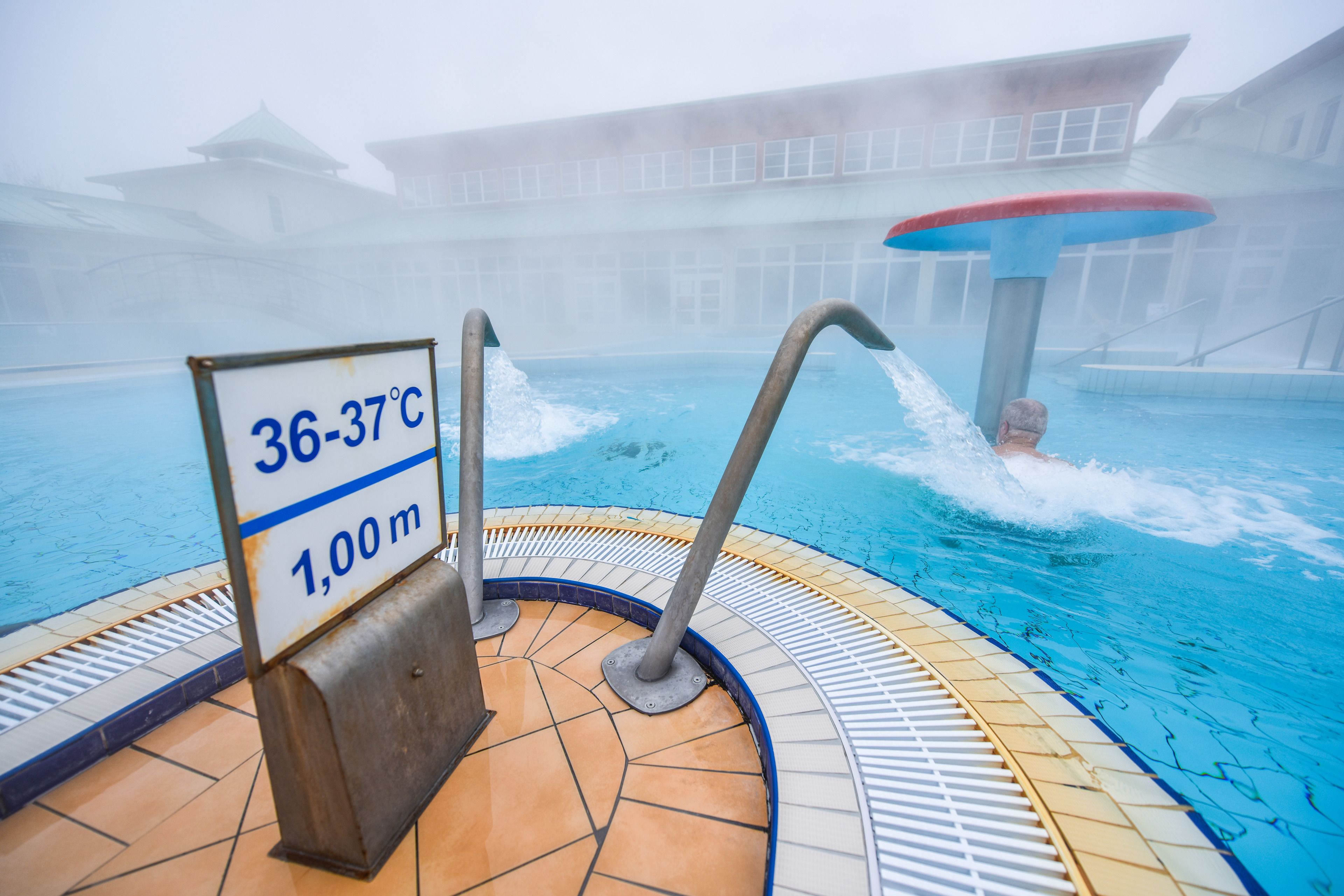 Ein Pool mit einem Hinweisschild für die Wassertemperatur, die 36 bis 37 Grad Celsius anzeigt, und einer angegebenen Tiefe von 1,00 Meter.