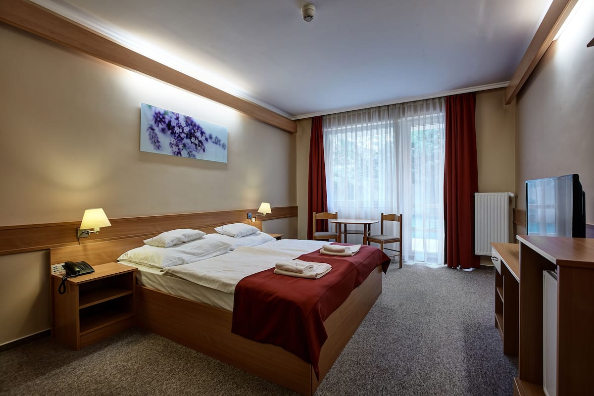 Ein Hotelzimmer mit einem Bett, Nachttischen, einem Schreibtisch, einem Sessel und einem Fernseher.