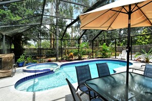 A covered outdoor swimming pool with a glass table and chairs, surrounded by potted plants and a wooden fence.