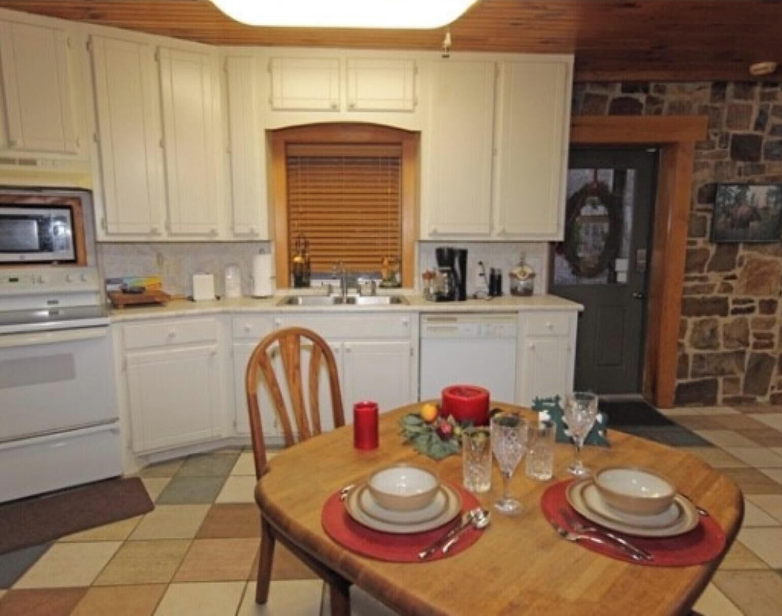 A kitchen with white cabinets, a microwave, an oven, a dining table set with plates, glasses, and cutlery.