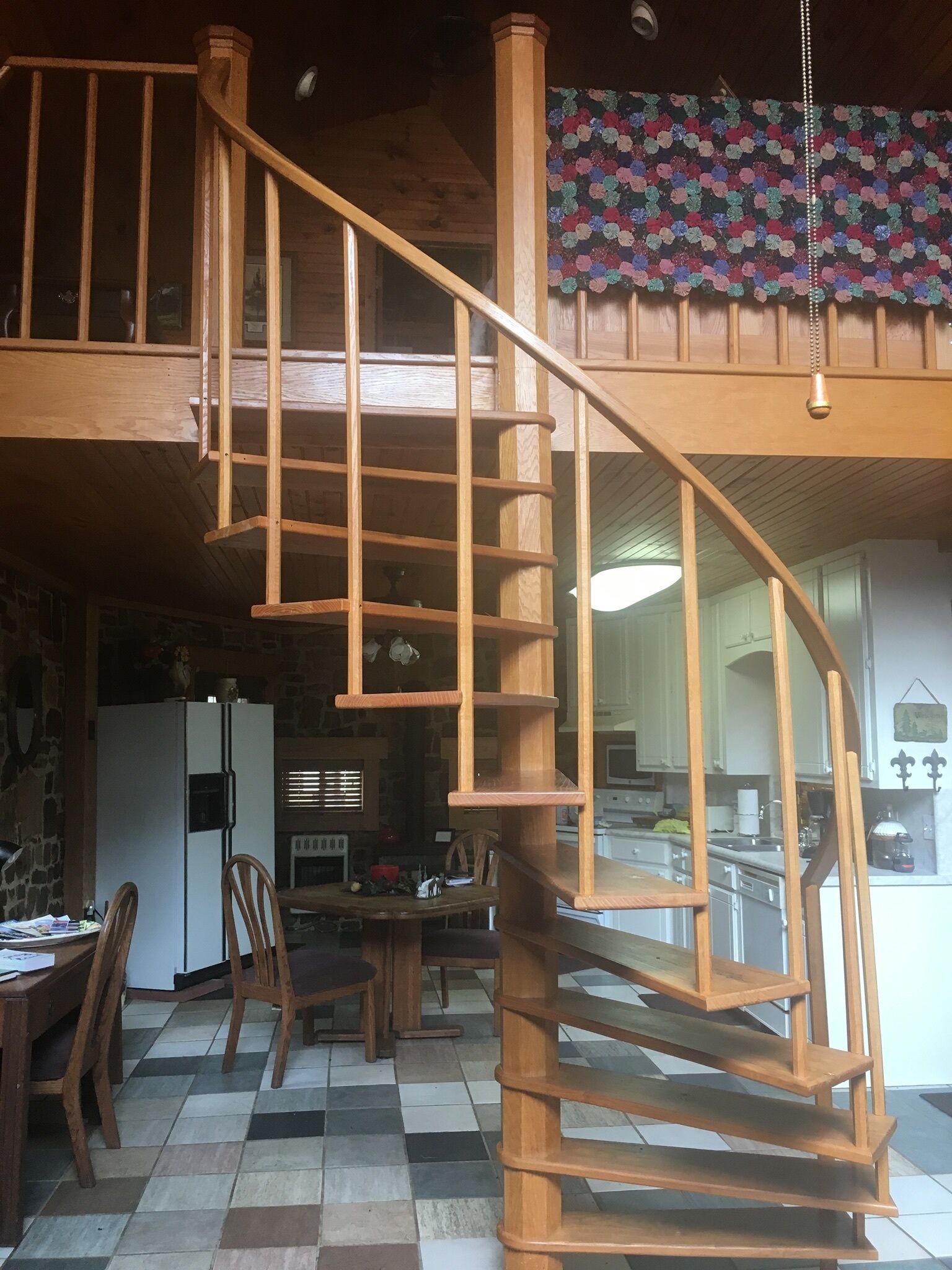 Eine Holztreppe führt zu einem Schlafbereich mit Schachbrettmuster und einer Küche im Hintergrund.