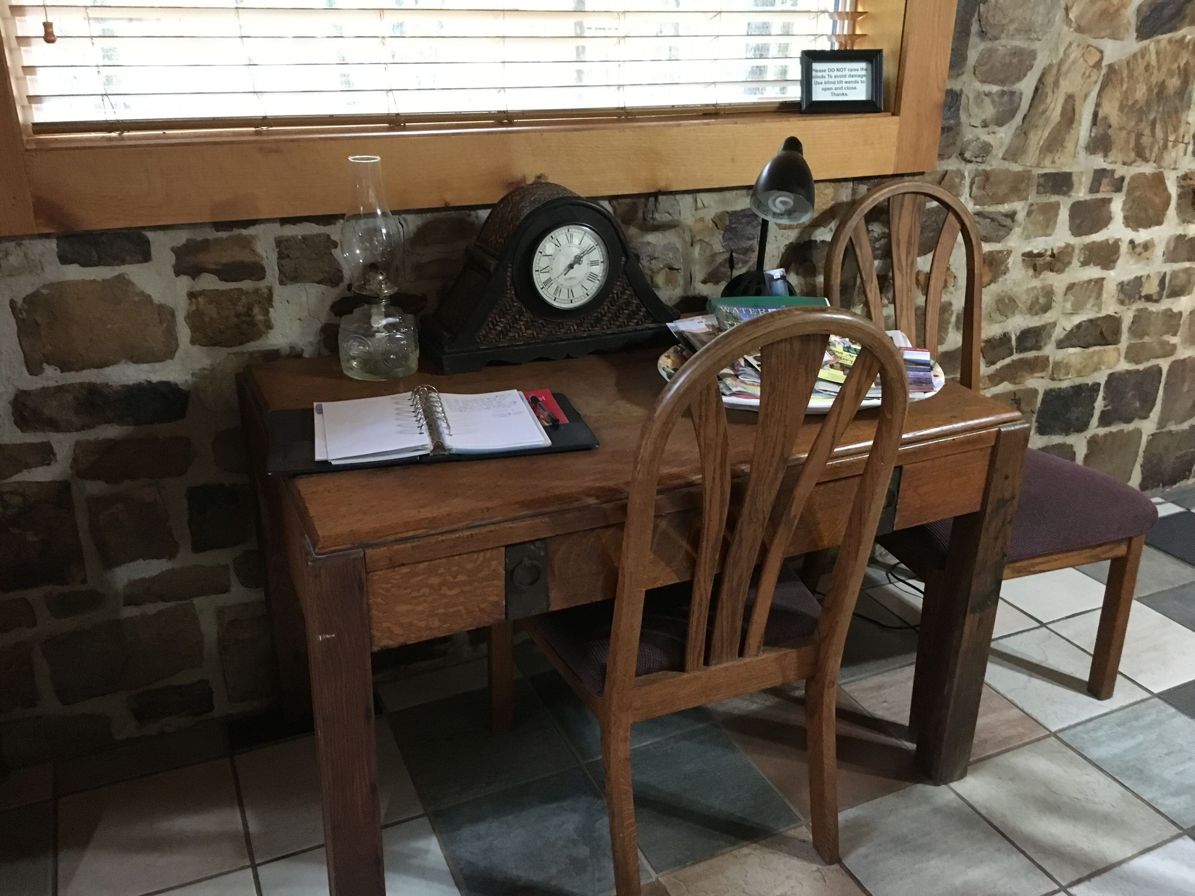 A wooden desk with a notebook, a clock, and a lamp.