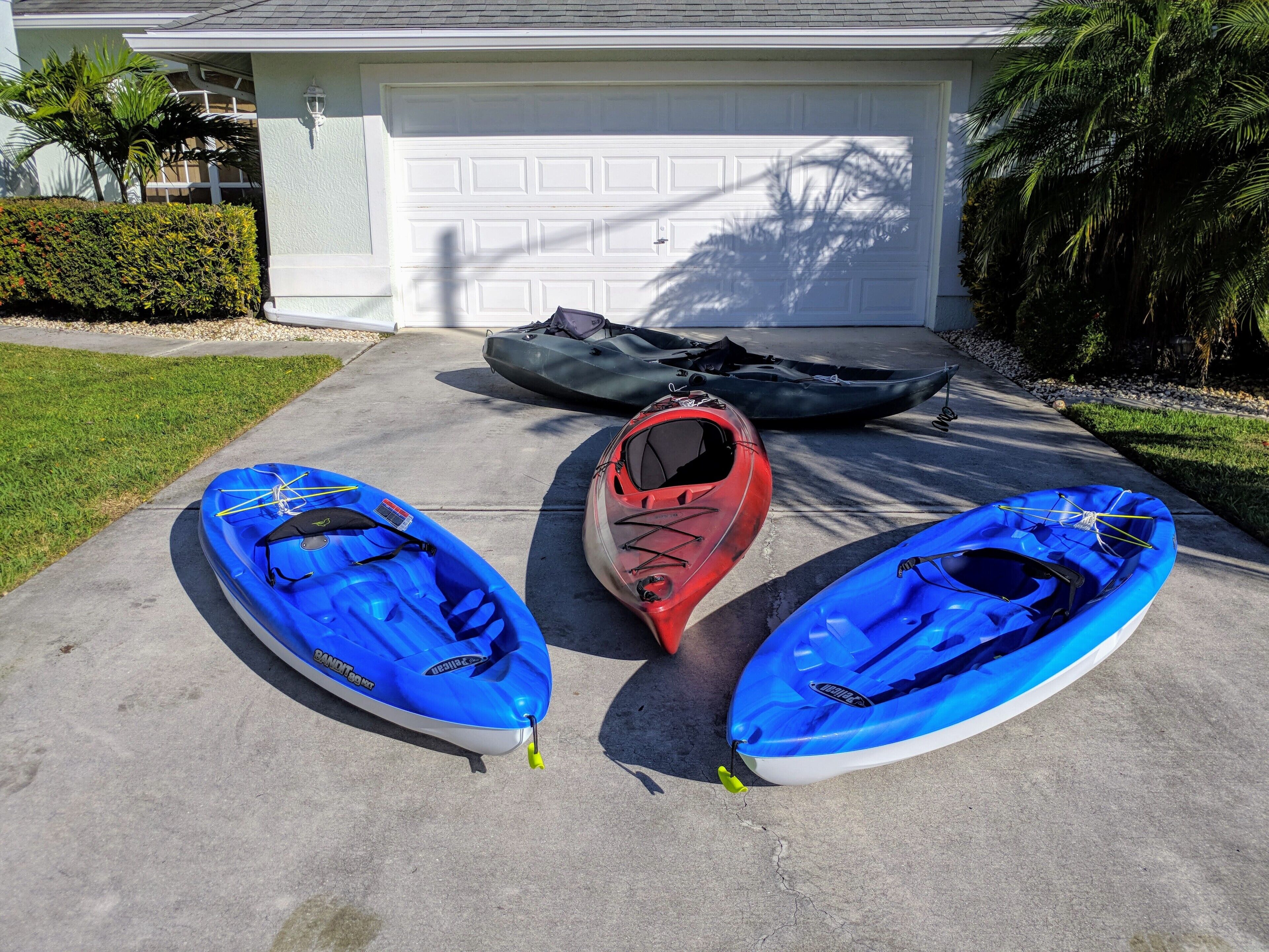 Tres kayaks sobre un camino de entrada frente a un garaje.