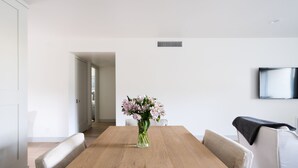 Un comedor moderno con una mesa de madera, un florero transparente con flores y un televisor montado en la pared.