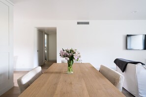 Zona pranzo moderna con tavolo in legno, vaso trasparente con fiori e televisore montato a parete.