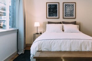 Un letto rifatto con lenzuola bianche, una lampada da comodino e due quadri appesi alla parete.