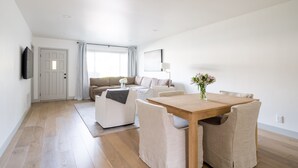 Una sala de estar moderna con una mesa de comedor de madera, sofás color beige y un televisor de pantalla plana montado en la pared.