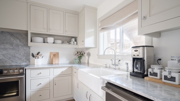Una cocina moderna con armarios blancos, encimera de mármol, electrodomésticos de acero inoxidable y una ventana que proporciona luz natural.
