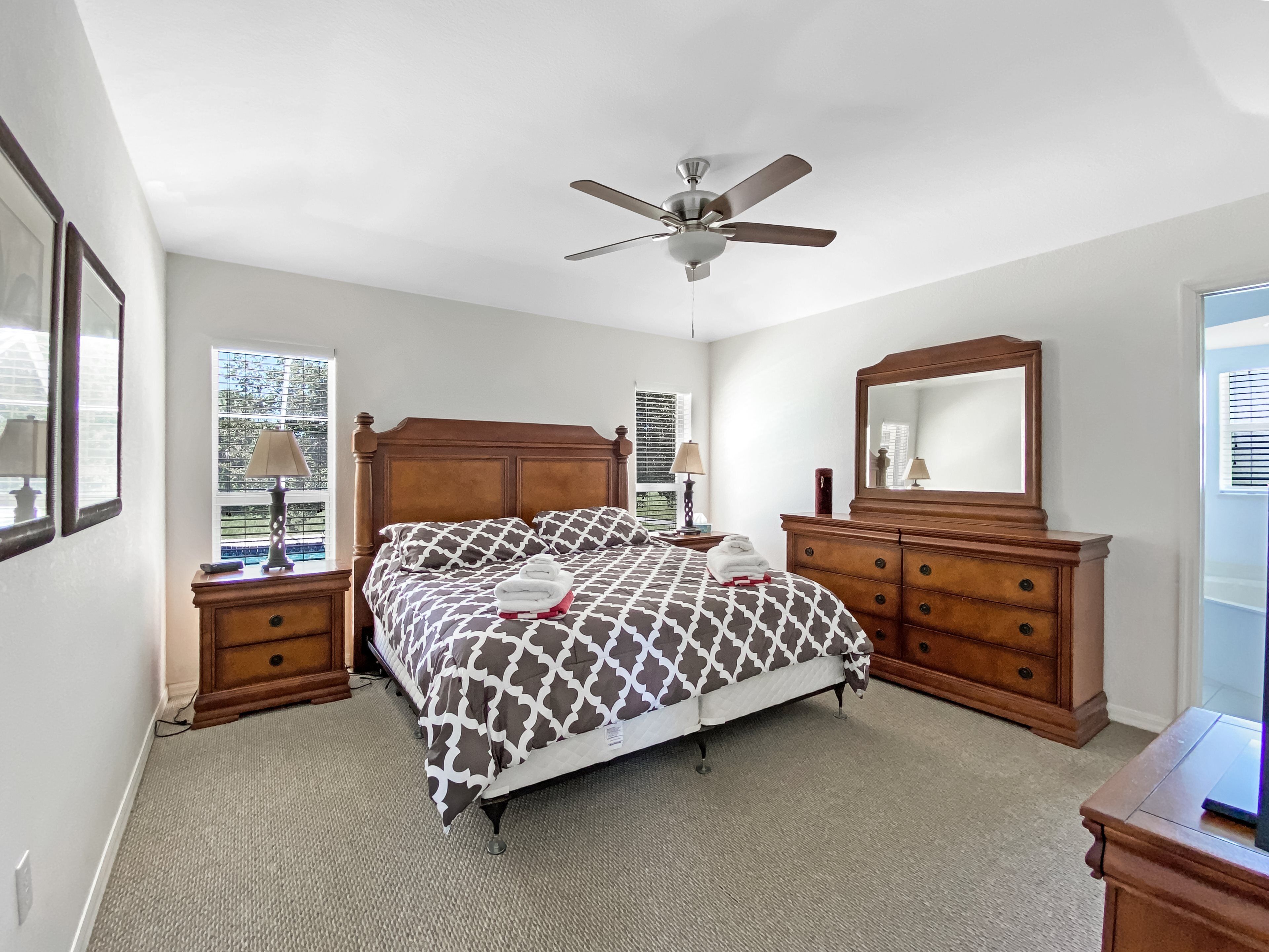 Une chambre à coucher comprenant un lit, une commode, un miroir, un ventilateur de plafond et une fenêtre.