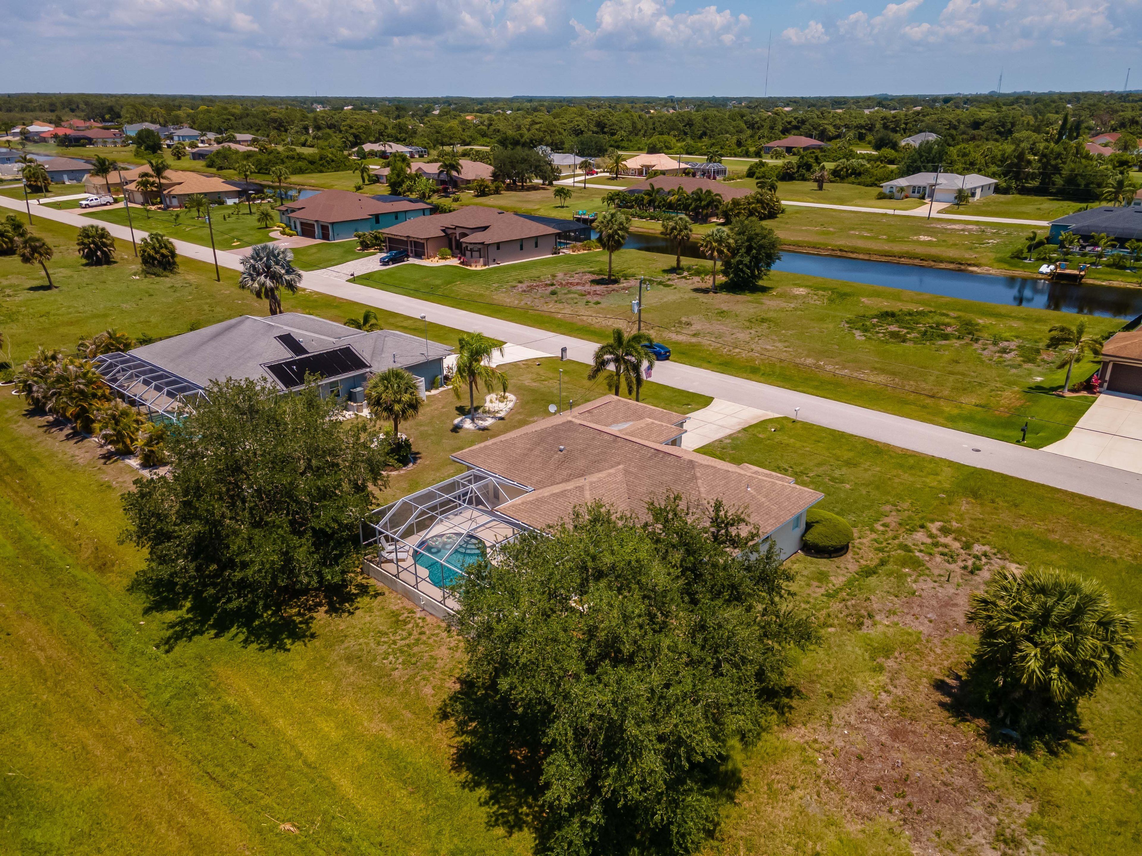 An aerial view of a residential area with houses, a swimming pool, and a small lake.