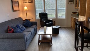A living room with a gray sofa, a black chair, a wooden coffee table, and a dining table with chairs.