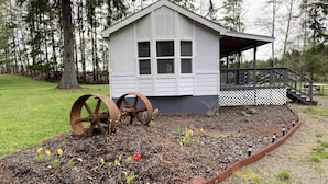 A small cabin with a porch, surrounded by a garden with mulch and flowers.