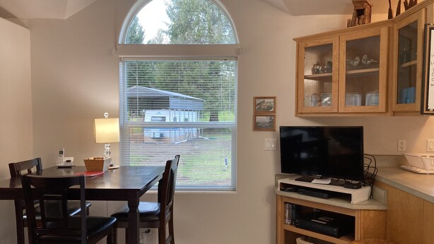 A dining area with a table and chairs, a television, and a cabinet with decorative items.