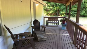A wooden deck with a bench and two chairs, a potted plant, and a railing.