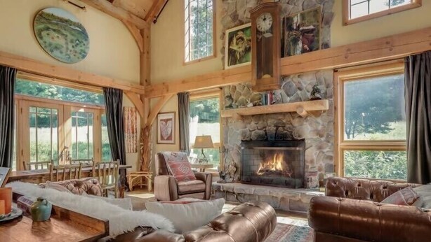 A cozy living room with a stone fireplace, leather sofas, and a wooden dining table. - WILLOW RUN LODGE  an Authentic Timber Frame Cabin on private 35 acres with river (Blakeslee)