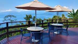A deck with outdoor seating, including round tables and chairs, and two umbrellas. - PARADISE! HOUSE IN ANGRA DOS REIS + BOAT FOR TOURS IN ILHA GRANDE (Angra dos Reis)