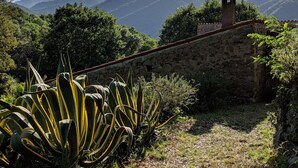 A stone wall with a small tower, surrounded by lush vegetation and mountains in the background.