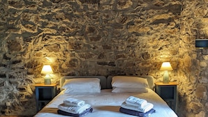 A room with a stone wall, a bed with white bedding, two bedside lamps, and a patterned rug.