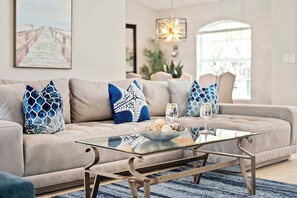 A modern living room with a beige sofa, blue patterned pillows, a glass coffee table, and a decorative light fixture. - Scarlett - Fantastic Rental with 2 King Size Beds (Cape Coral)