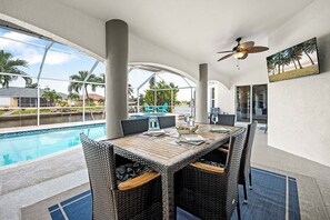 An outdoor dining area with a pool, wicker furniture, and a ceiling fan.