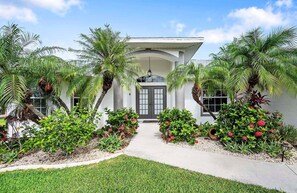 A modern building with a central entrance, surrounded by lush greenery and flowering plants. - Scarlett - Fantastic Rental with 2 King Size Beds (Cape Coral)